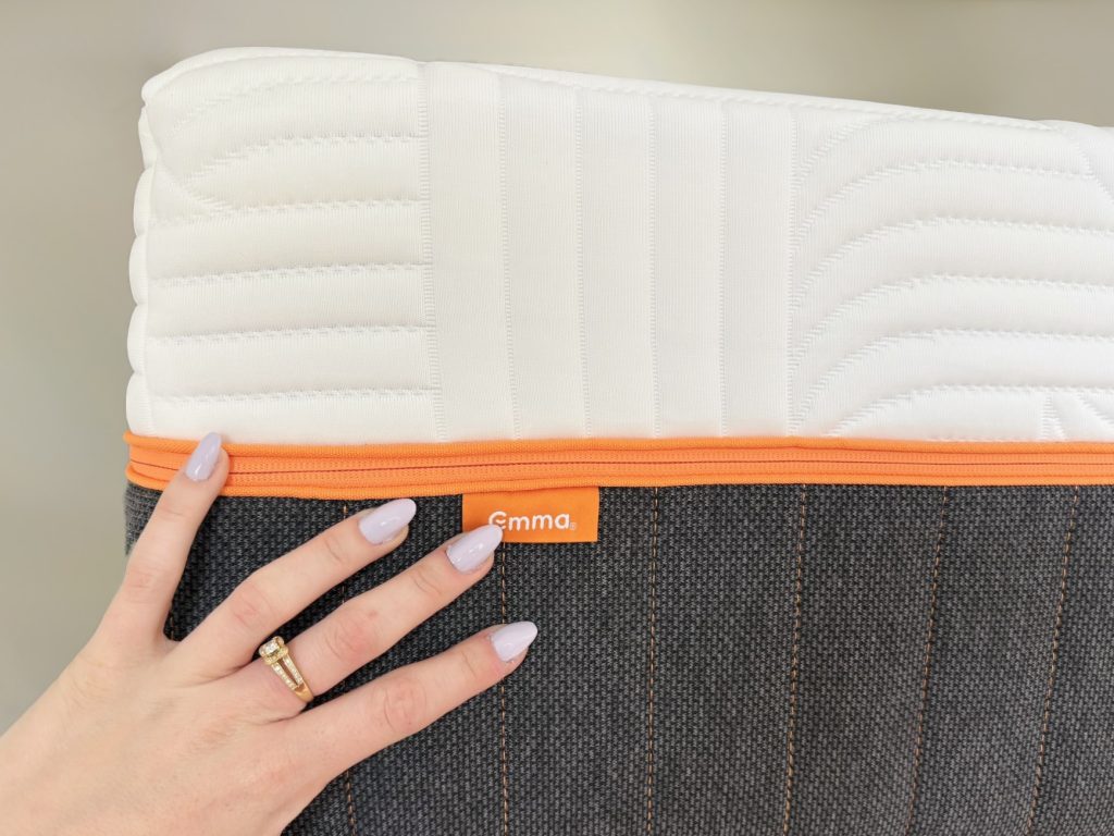 Emma Performance matras, hand op de oranje bies en de grijze onderhoes met Emma-label